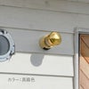 白い住宅の壁に、真鍮色のライトが取り付けられている。ガラスがくもっていて、中の電球は見えない。