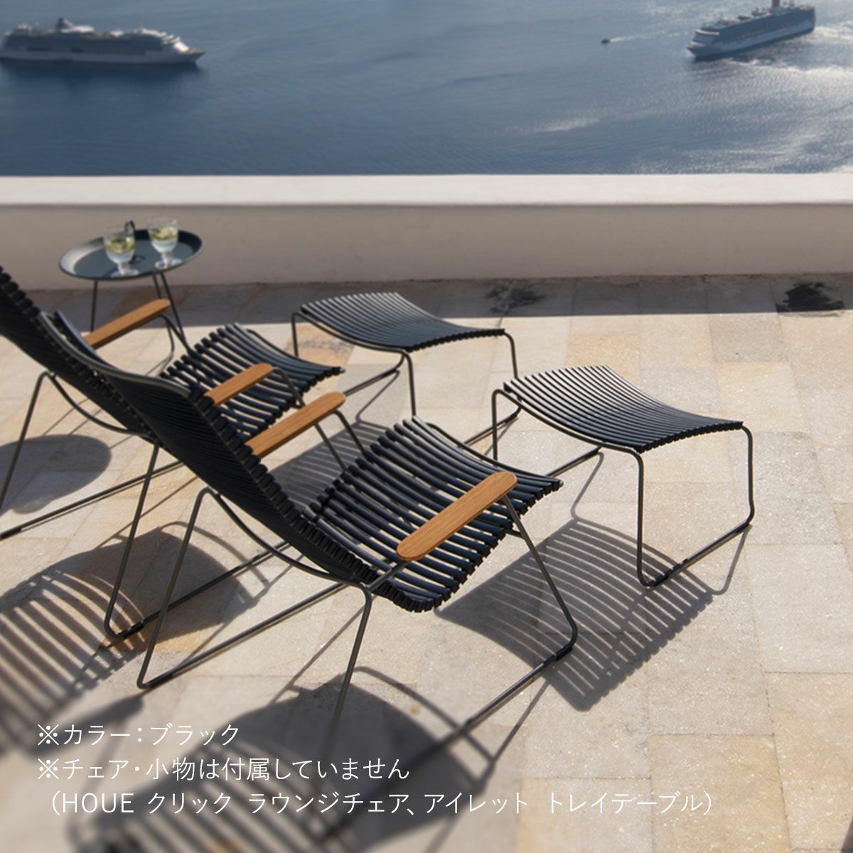 屋外のデッキにブラックのフットレスト2個とチェア2脚とテーブルの画像です。本商品には、チェアとテーブル小物は付属していません。